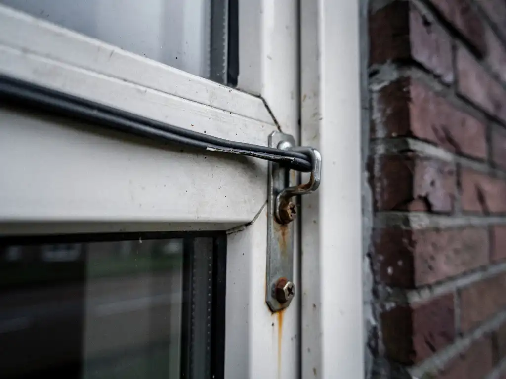 Verouderd wit PVC-raamkozijn met vervormd afdichtingsrubber en gebogen sluiting in bakstenen gevel, tekenen van tochtverlies.