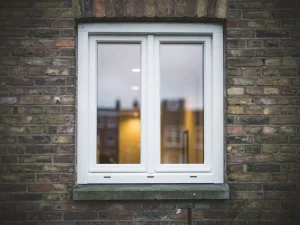 Wit uPVC raamkozijn in bakstenen gevel van Hollandse rijtjeswoning met warm binnenverlichting door driedubbel glas.