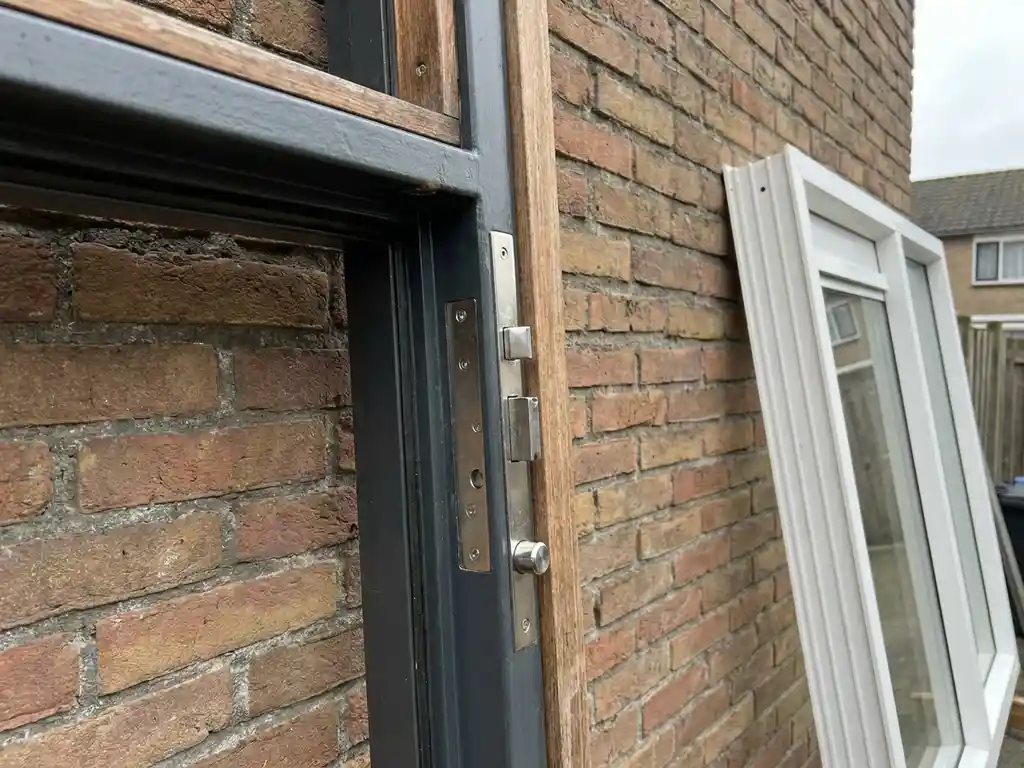 Inbraakwerend raamkozijn met zichtbare stalen sluitingsmechanismen in Nederlandse bakstenen gevel, wit kunststof kozijn tegen de muur.