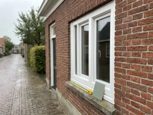 Wit PVC-kozijn gemonteerd in traditionele rode bakstenen gevel in Sneek, met meetlint en materiaalstaal op de vensterbank.