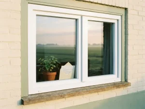 Nieuw wit PVC-kozijn in de gevel van een Nederlandse polderwoning, met een subsidiebeschikking op de vensterbank en agrarisch landschap door het glas.