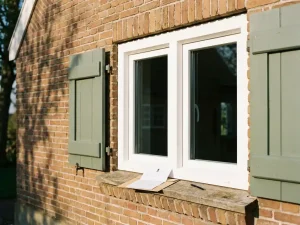 Nieuw wit PVC-raamkozijn in Friese bakstenen gevel met subsidiedocument en pen op de vensterbank in middagzon.