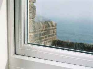 Waterdruppels op een wit uPVC kozijn met verweerde bakstenen muur op de achtergrond in kustmist.